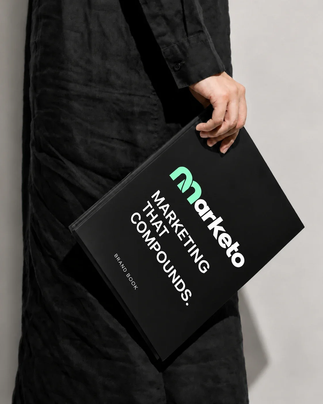 A hand holding the Marketo brand book, titled Marketing that compounds